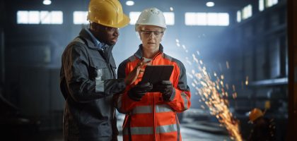 Engineers Stand in Steel Metal Manufacturing Factory, Use Digital Tablet Computer and Have a Discussion